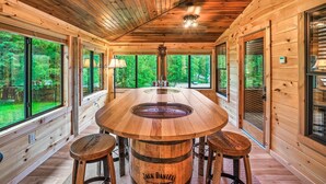 A wooden interior with a central barrel table, large windows, and a view of the forest. - Luxury Smokies Home with Backyard Paradise (Sevierville)