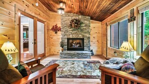 A cozy log cabin interior with a stone fireplace, wooden walls, and a large window. - Luxury Smokies Home with Backyard Paradise (Sevierville)