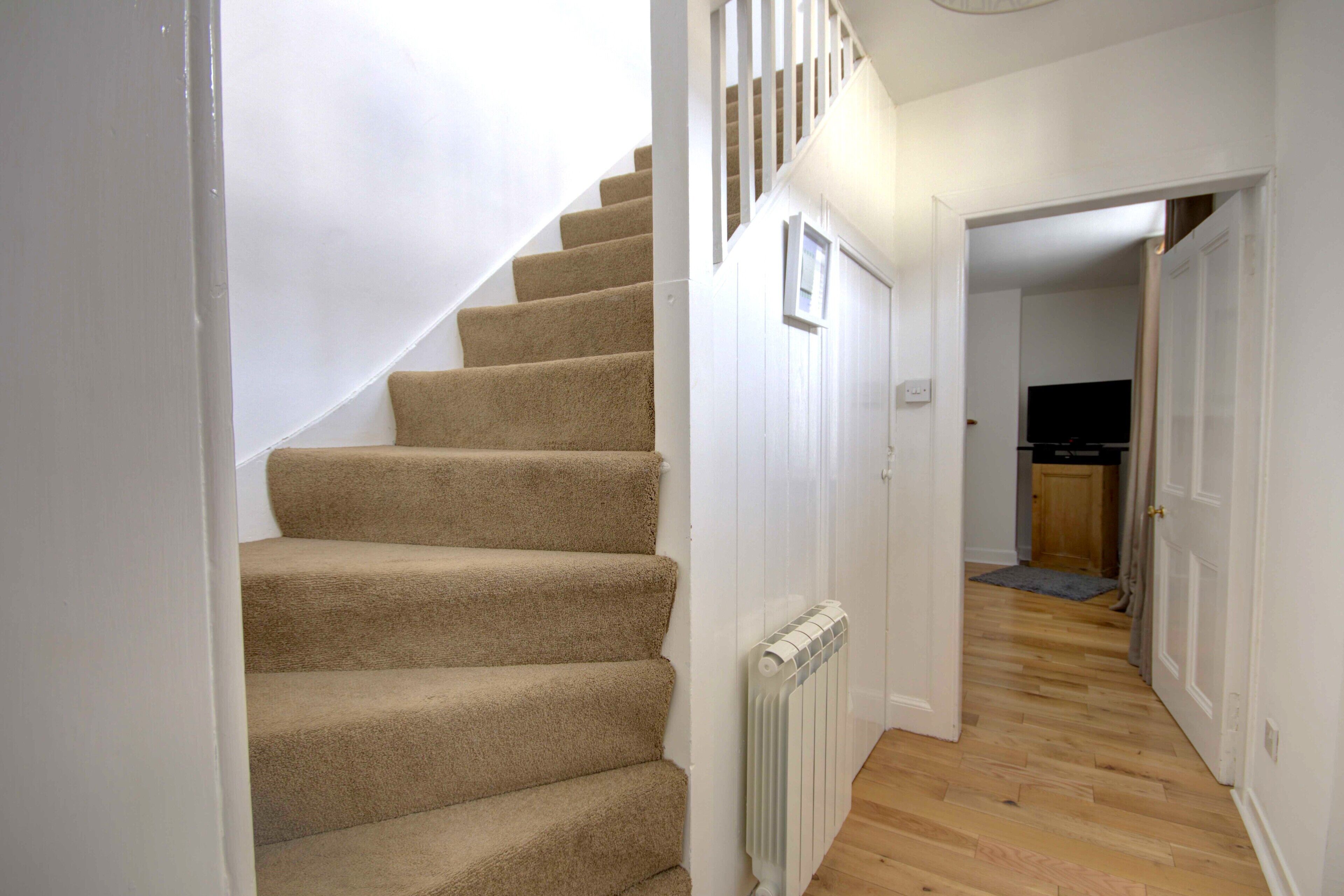 A staircase with carpeted steps leading to a landing, a white radiator, and a wooden floor.