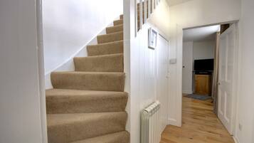 A staircase with carpeted steps leading to a landing, a white radiator, and a wooden floor.