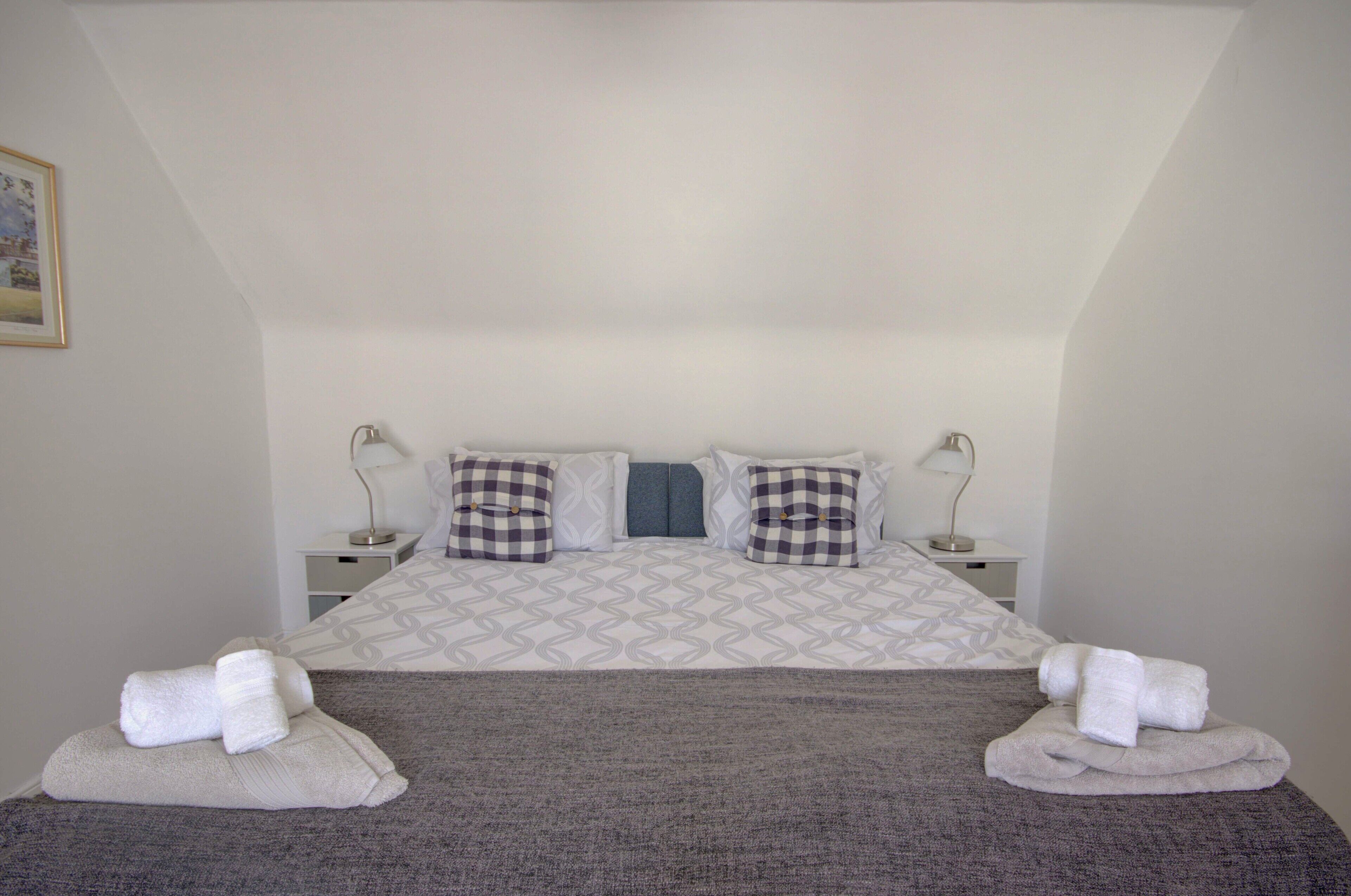 Un lit bien fait, recouvert d’une couvre-lit à motifs, avec deux oreillers et deux tables de chevet dotées de lampes.