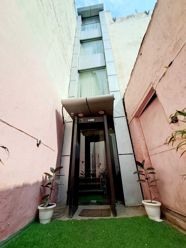 A hotel entrance with a modern design, featuring a glass door, a small outdoor area with artificial grass, and potted plants. - Hotel Diamond Airport (New Delhi)