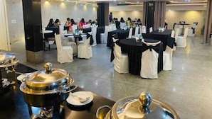 Un salón de banquetes con mesas redondas, fundas blancas en las sillas y servicio de buffet.