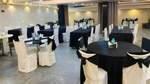 Un salón de banquetes con mesas redondas y sillas, algunas con manteles negros y cubre-sillas blancos.