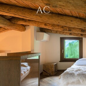 A rustic bedroom with a wooden ceiling, a bed with a white furry cover, a small bedside table, and a window with a view of greenery. - Ecobaita del Cacciatore (Incudine)