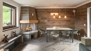 A cozy dining area with a stone fireplace, wooden walls, and a view of greenery outside. - Ecobaita del Cacciatore (Incudine)