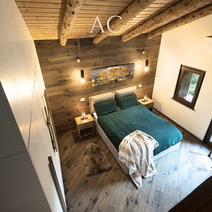 A bedroom with a wooden ceiling, a bed with green bedding, a painting above the bed, and a window on the right side. - Ecobaita del Cacciatore (Incudine)
