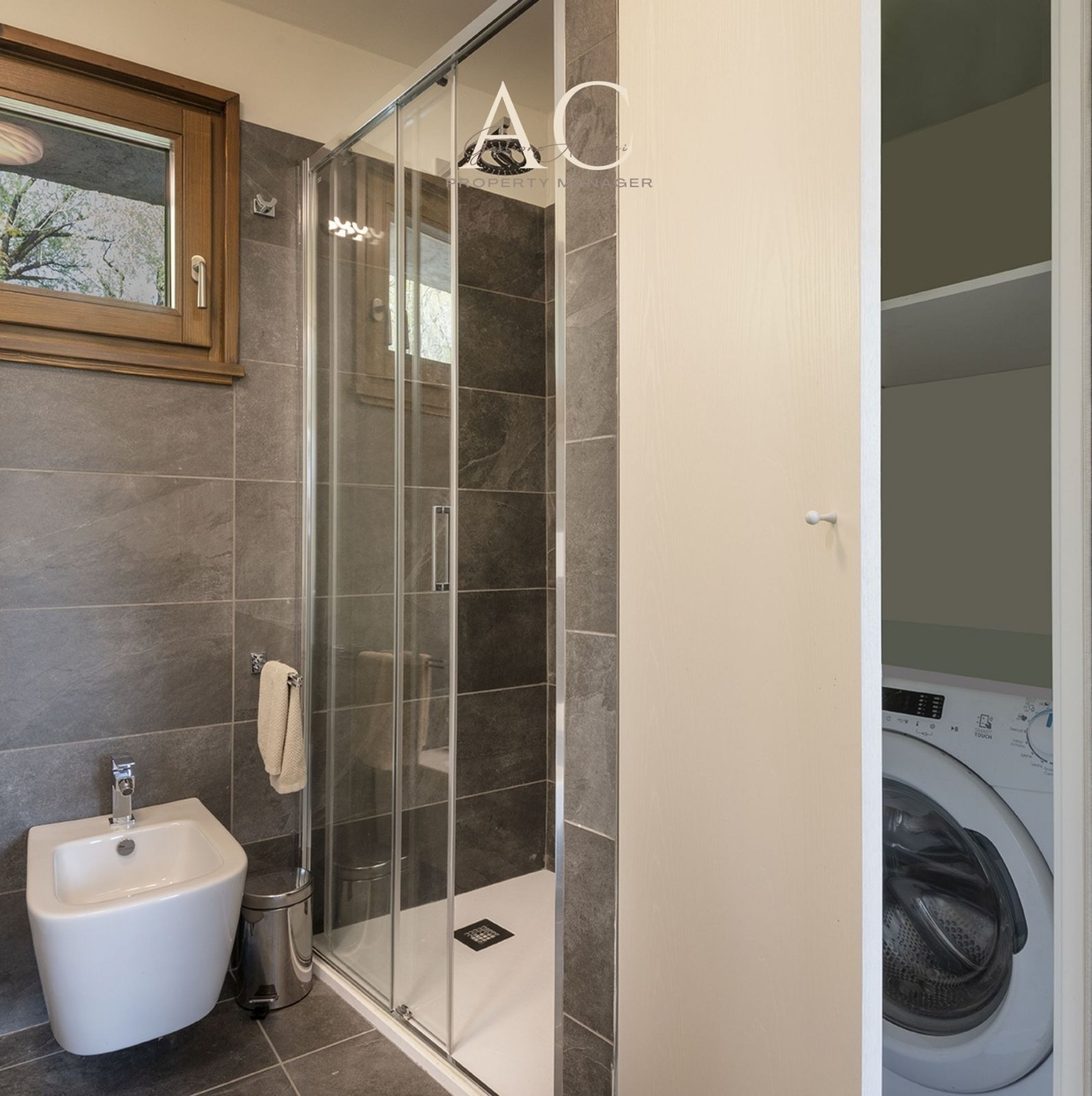A modern bathroom with a glass shower enclosure, a white pedestal sink, and a washing machine in the adjacent room.