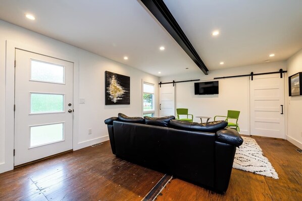 Un salon moderne avec un canapé en cuir noir, des fauteuils verts, un téléviseur à écran plat et un grand tableau abstrait.