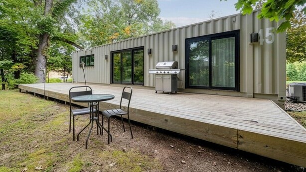 A modern outdoor deck with a grill, a table, and chairs. - Unique container home retreat near Lake Michigan. Enjoy a peaceful, private setting with a spacious deck, firepit, and ravine views. Close to beaches, wineries, and downtown St. Joseph—perfect for a relaxing Southwest Michigan getaway. (Benton Harbor)