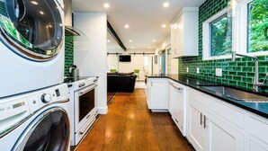 A modern kitchen with a built-in washer and dryer, a wooden floor, and a green-tiled backsplash. - Unique container home retreat near Lake Michigan. Enjoy a peaceful, private setting with a spacious deck, firepit, and ravine views. Close to beaches, wineries, and downtown St. Joseph—perfect for a relaxing Southwest Michigan getaway. (Benton Harbor)