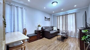 Una sala de estar moderna con piso de madera, un sofá, una mesa de centro, una mesa de comedor con sillas y un televisor.