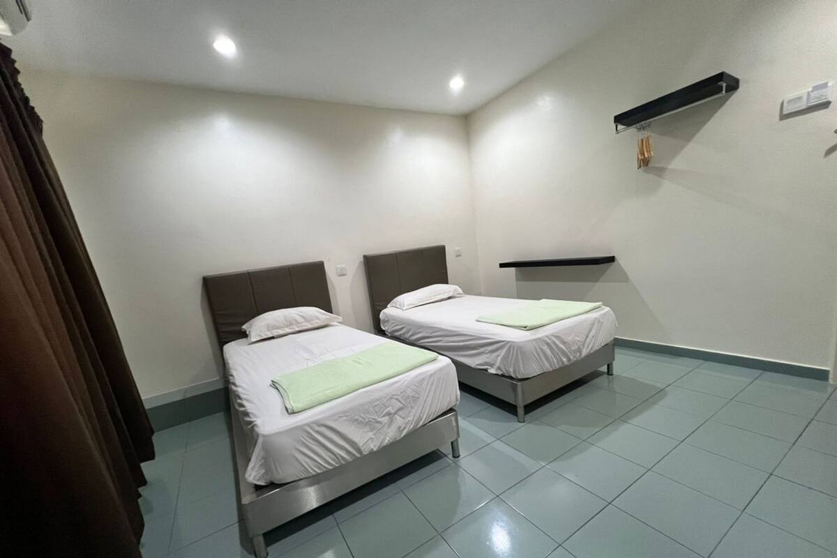 Una habitación de hotel con dos camas individuales, un pequeño estante con artículos de aseo y suelo de baldosas.