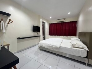 Une chambre d’hôtel avec un lit, un téléviseur fixé au mur, une petite table et une fenêtre avec un rideau rouge.