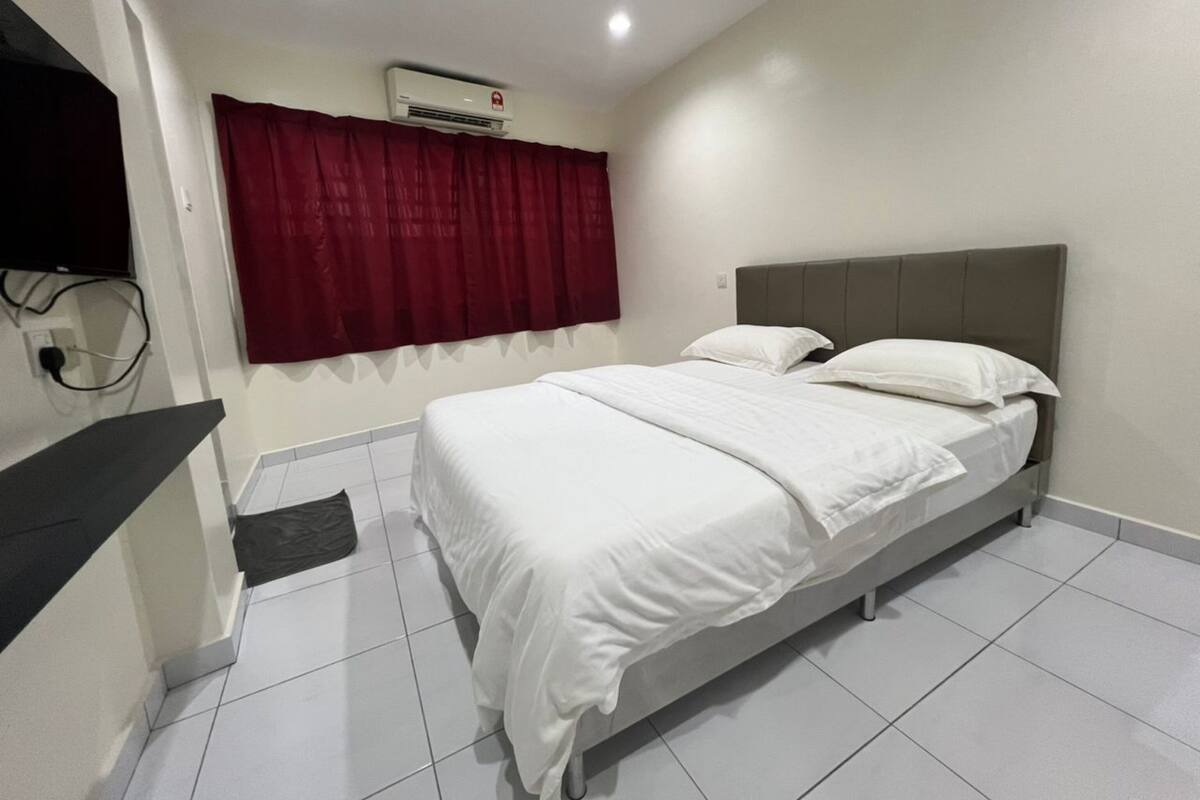 Habitación de hotel con una cama, televisor montado en la pared y un equipo de aire acondicionado sobre la cama.