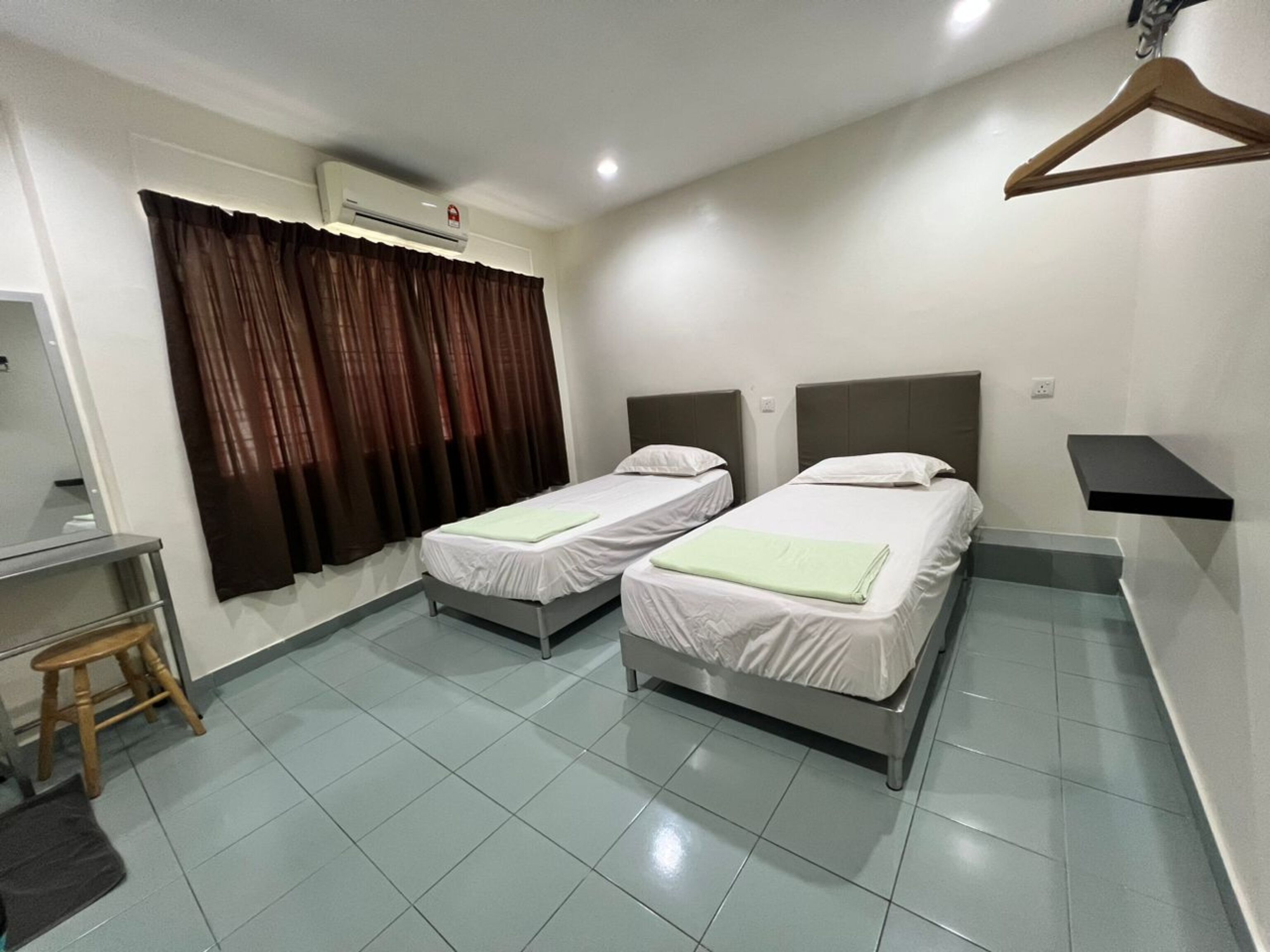 A hotel room with two single beds, a desk, a chair, a hanging coat rack, and a window with curtains.