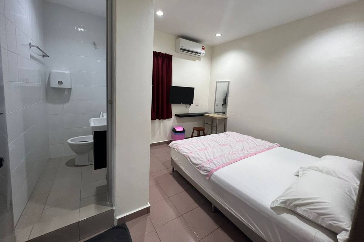 Habitación de hotel con cama, escritorio, silla, televisión, espejo y baño con inodoro y ducha.