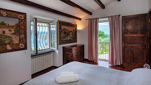 A bedroom with a large bed, a dresser, and a window with a view of the sea.