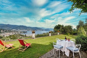 A terrace with a table set for dining, red chairs, and a view of a lake and mountains.