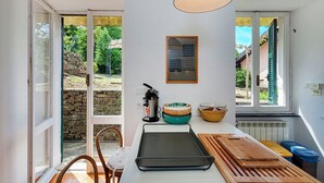 A kitchen with a large window, a hanging light fixture, and a stone wall visible through the glass door.