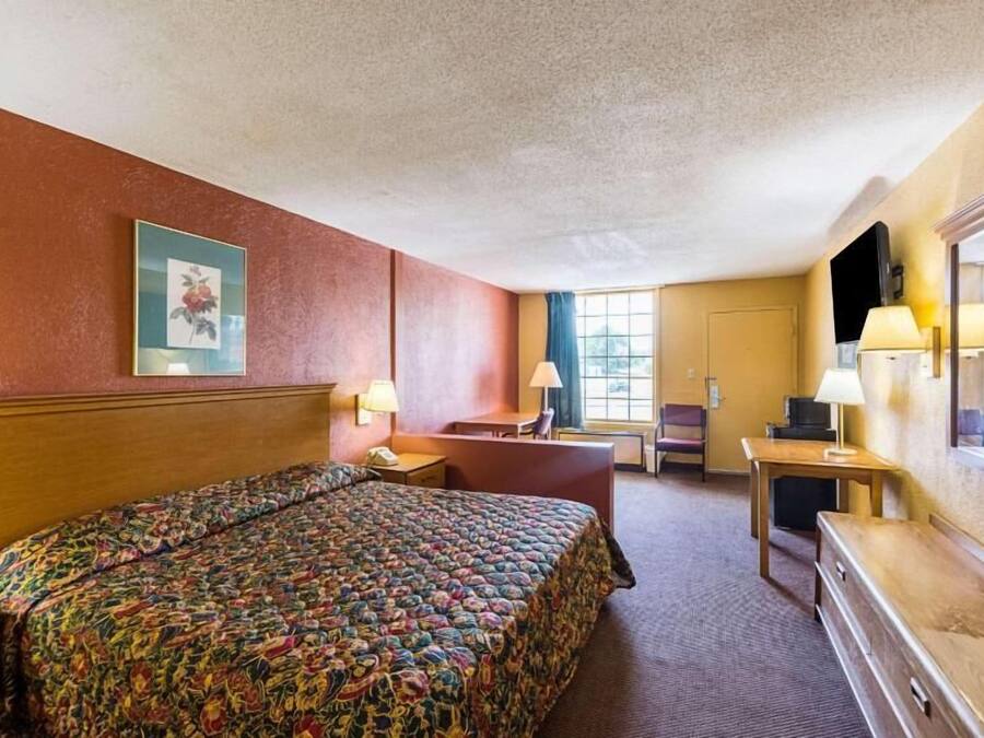 A hotel room with a large bed, a desk, a chair, a TV, and a window with curtains.