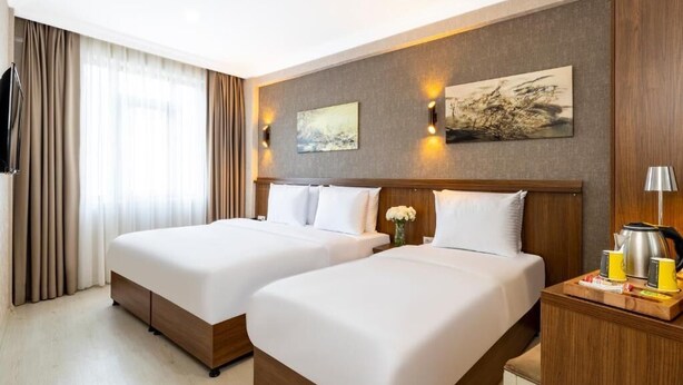 A hotel room with two beds, a wooden headboard, a flat-screen TV, a painting, and a bedside table with a kettle and cups. - Diamond Beyazıt Hotel (Istanbul)