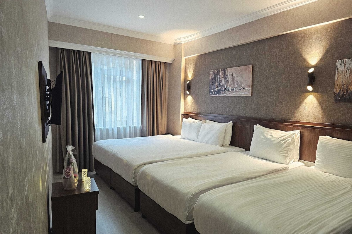 A hotel room with two beds, a TV, a painting, and a nightstand with a vase.