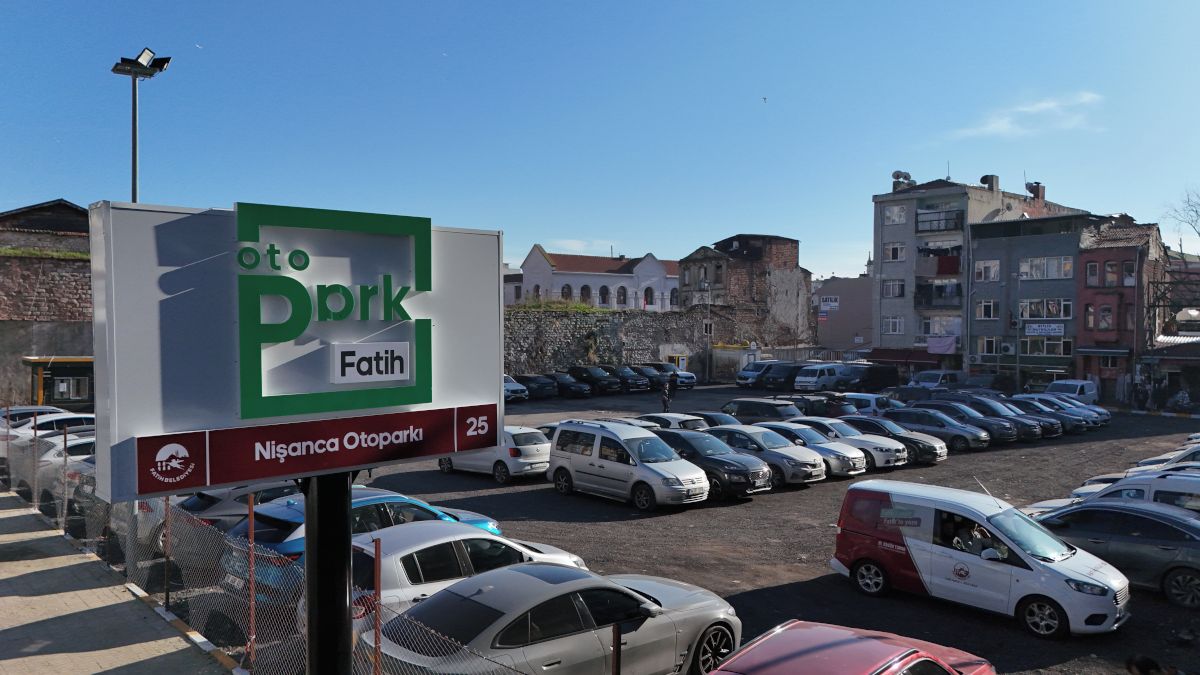 En parkeringsplads med flere biler, et skilt med 'oto Pprk Fatih' og bygninger i baggrunden.