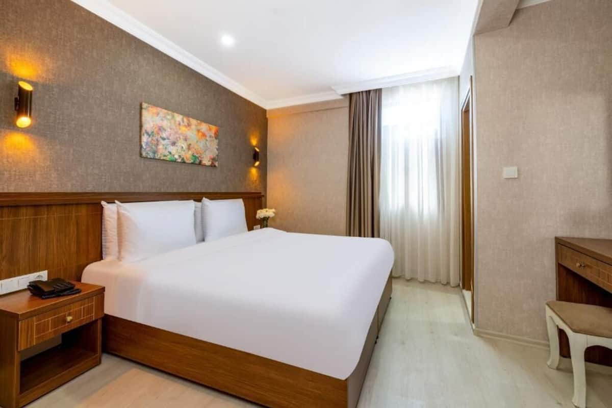 A hotel room with a large bed, wooden headboard, bedside table, and a desk with a chair.