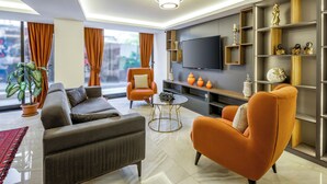 A modern living room with a sofa, armchair, and coffee table. There is a TV mounted on the wall and a bookshelf with decorative items. - Diamond Beyazıt Hotel (Istanbul)