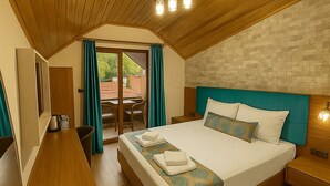 Un dormitorio con techo de madera, una cama con colcha estampada, una mesita de noche y vistas al exterior a través de un ventanal corredero.