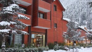 Un edificio rojo con balcón, rodeado de árboles nevados y un paisaje montañoso.