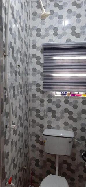 A small bathroom with a toilet, shower, and a window with blinds. - Inertia Place - Lovely 1 Bedroom Apertment (Lagos)