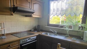Une cuisine avec des meubles de rangement en bois, une cuisinière, un évier et une fenêtre ornée de rideaux en dentelle.