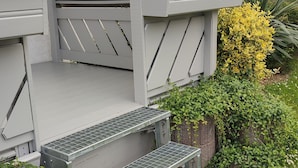 Une maison à l’extérieur gris, avec un petit porche doté de quelques marches et une fenêtre ornée d’un rideau en dentelle.