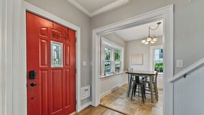 A hallway with a red door, a dining area with a table and chairs, and a chandelier. - Cozy Corner Cottage| Beach Access & Historic Charm (Sheboygan)