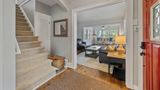 A staircase leading to a living area with a red door, a wooden floor, and a view into the adjacent room. - Cozy Corner Cottage| Beach Access & Historic Charm (Sheboygan)