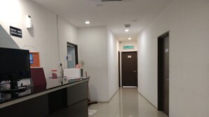 Zona de recepción de hotel con mostrador de entrada, un cartel que indica los horarios de registro, un letrero de salida KELUAR y un piso de baldosas limpias.