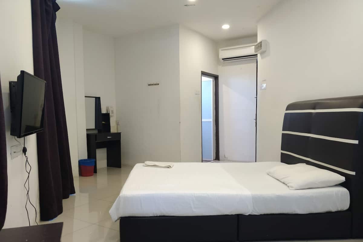 A hotel room with a bed, a desk, a television, and an air conditioning unit.