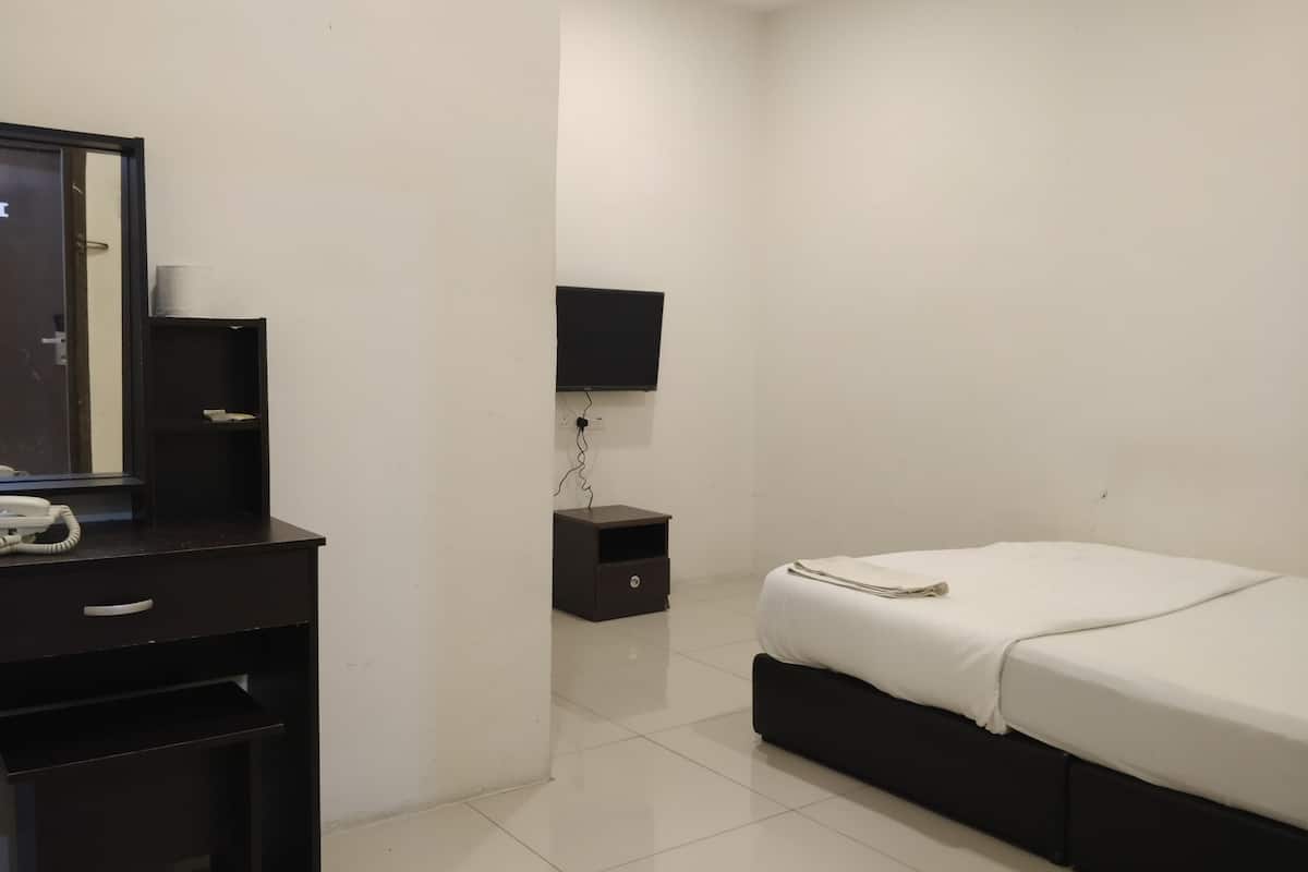 A small, clean room with a bed, a desk with a telephone, a TV mounted on the wall, and a small nightstand.