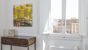 A room with a white wall, a wooden table with drawers, a radiator, and a window with a view of buildings. - Trastevere 900 Liberty (Roma)