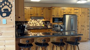 A modern kitchen with wooden cabinets, a stainless steel refrigerator, and a bar area with stools. - Granite Lake Chalet - waterfront Temagami/Hot Tub (Temagami)