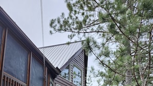 A cabin with a wooden deck, a staircase leading to a second level, and a large air conditioning unit on the ground. - Granite Lake Chalet - waterfront Temagami/Hot Tub (Temagami)