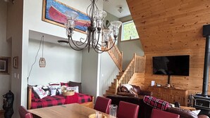 A wooden interior with a dining table, red chairs, a chandelier, a sofa, and a television. - Granite Lake Chalet - waterfront Temagami/Hot Tub (Temagami)