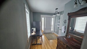 A hallway with a wooden floor, a black table with a coffee maker, a mirror, and a dresser. - DuBois' Inn (Madawaska)