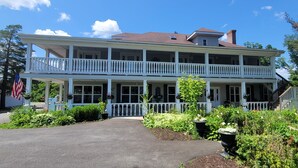 A two-story building with a balcony, a flag, and a well-maintained garden. - DuBois' Inn (Madawaska)
