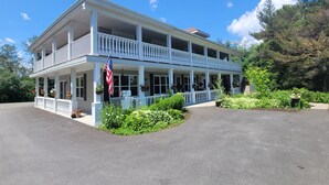 A two-story building with a balcony, surrounded by greenery and an American flag. - DuBois' Inn (Madawaska)