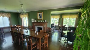 A dining room with a wooden table and chairs, a fireplace, and large windows with curtains. - DuBois' Inn (Madawaska)