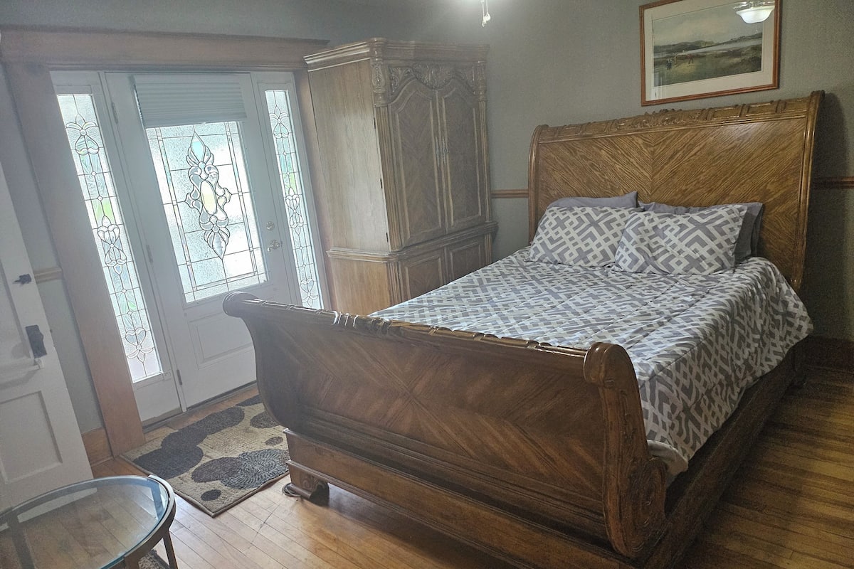 A bedroom with a wooden bed, a glass table, and a door with stained glass windows.