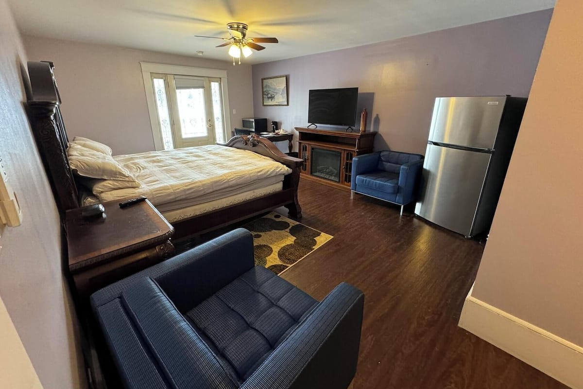 A bedroom with a bed, a desk, a chair, a television, and a refrigerator.